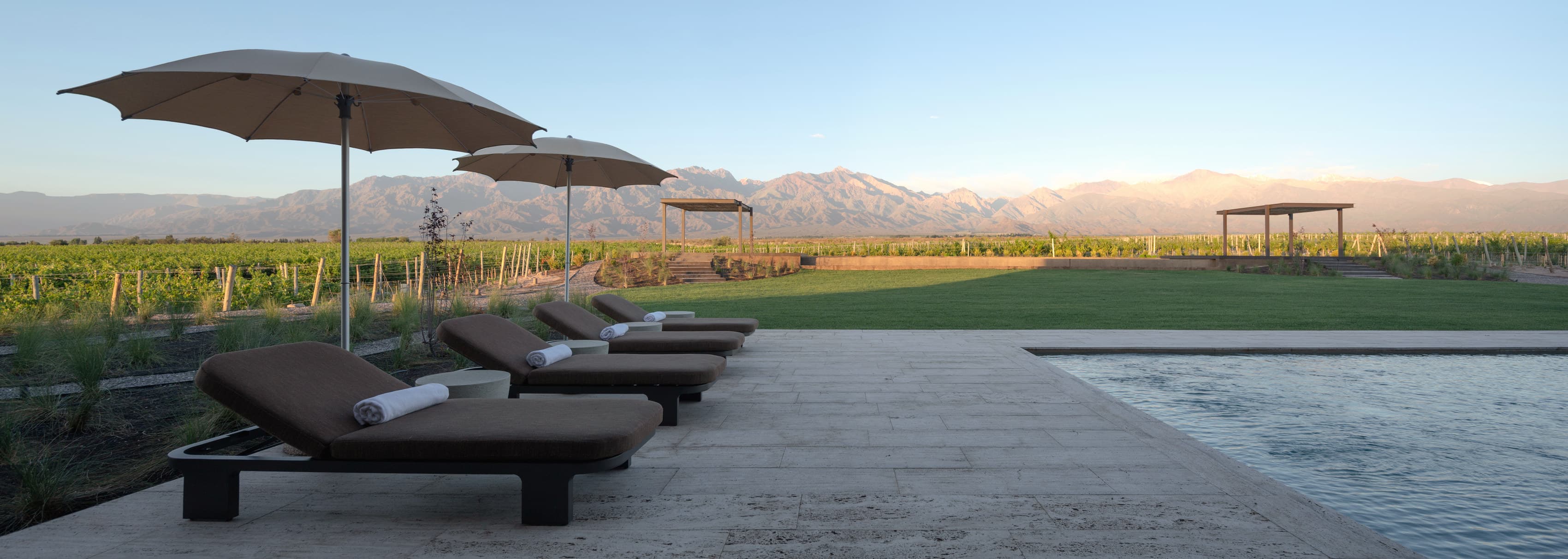 Deck de travertino junto a la pileta al atardecer, con el viñedo y la cordillera detrás