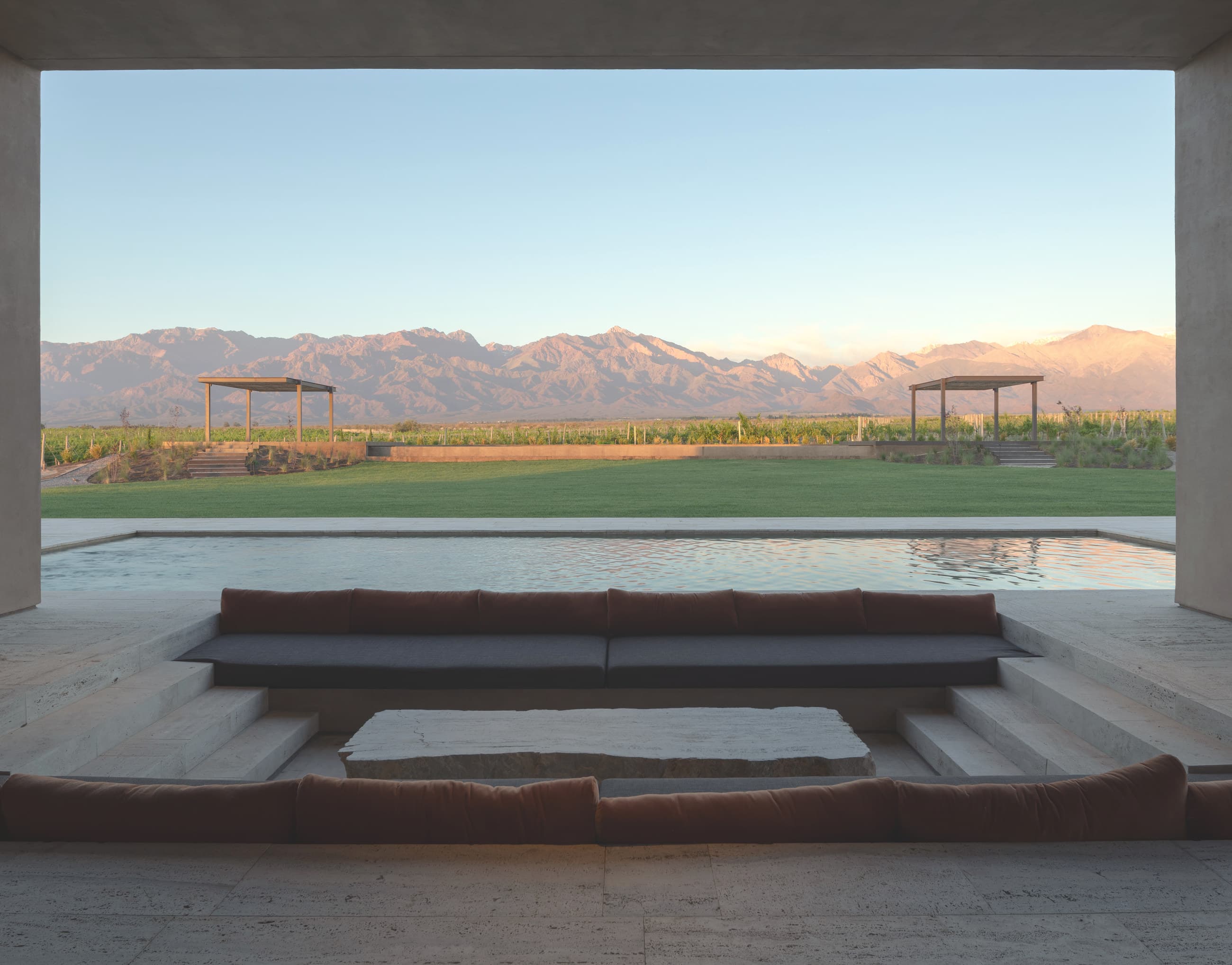 Galería con solado de travertino frente a una pileta, con los viñedos y la cordillera al fondo