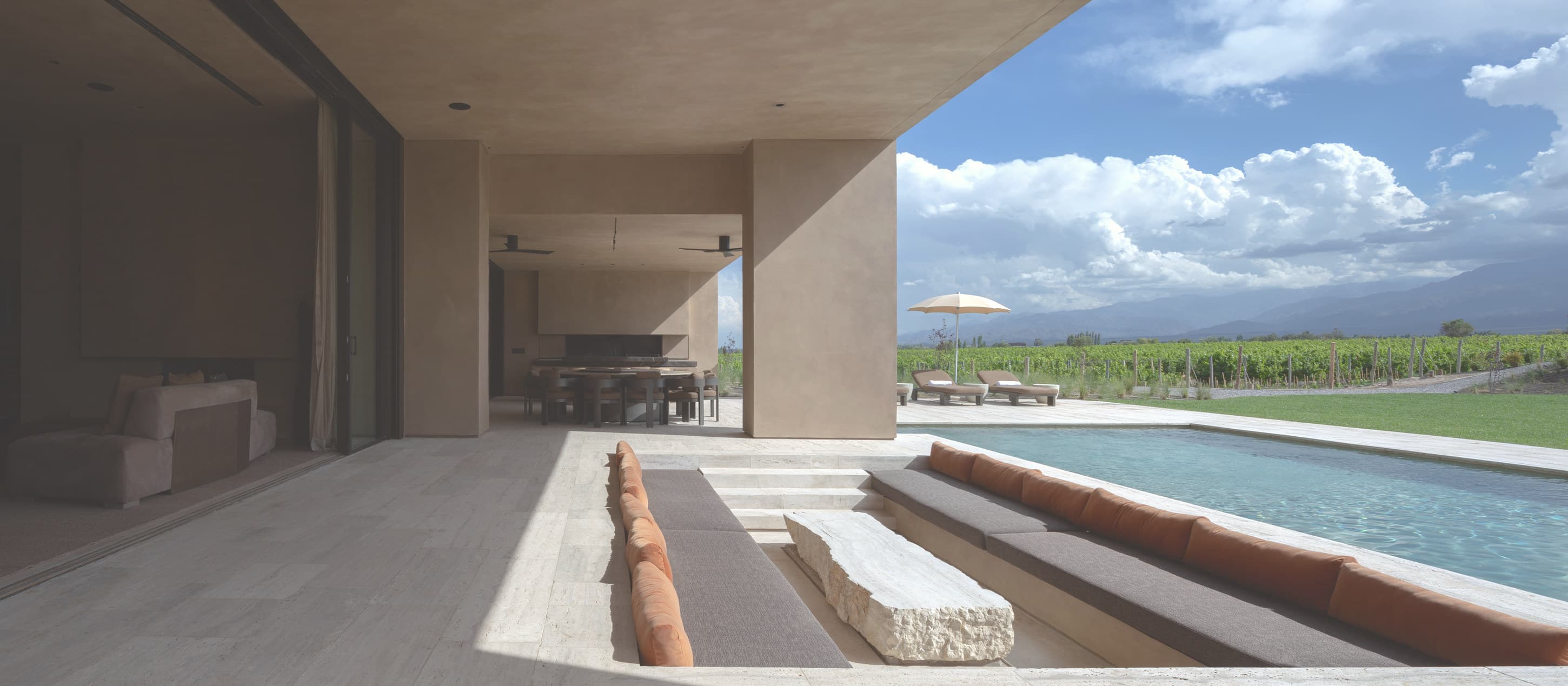 Galería de travertino con banco macizo, abierta a la pileta y al viñedo