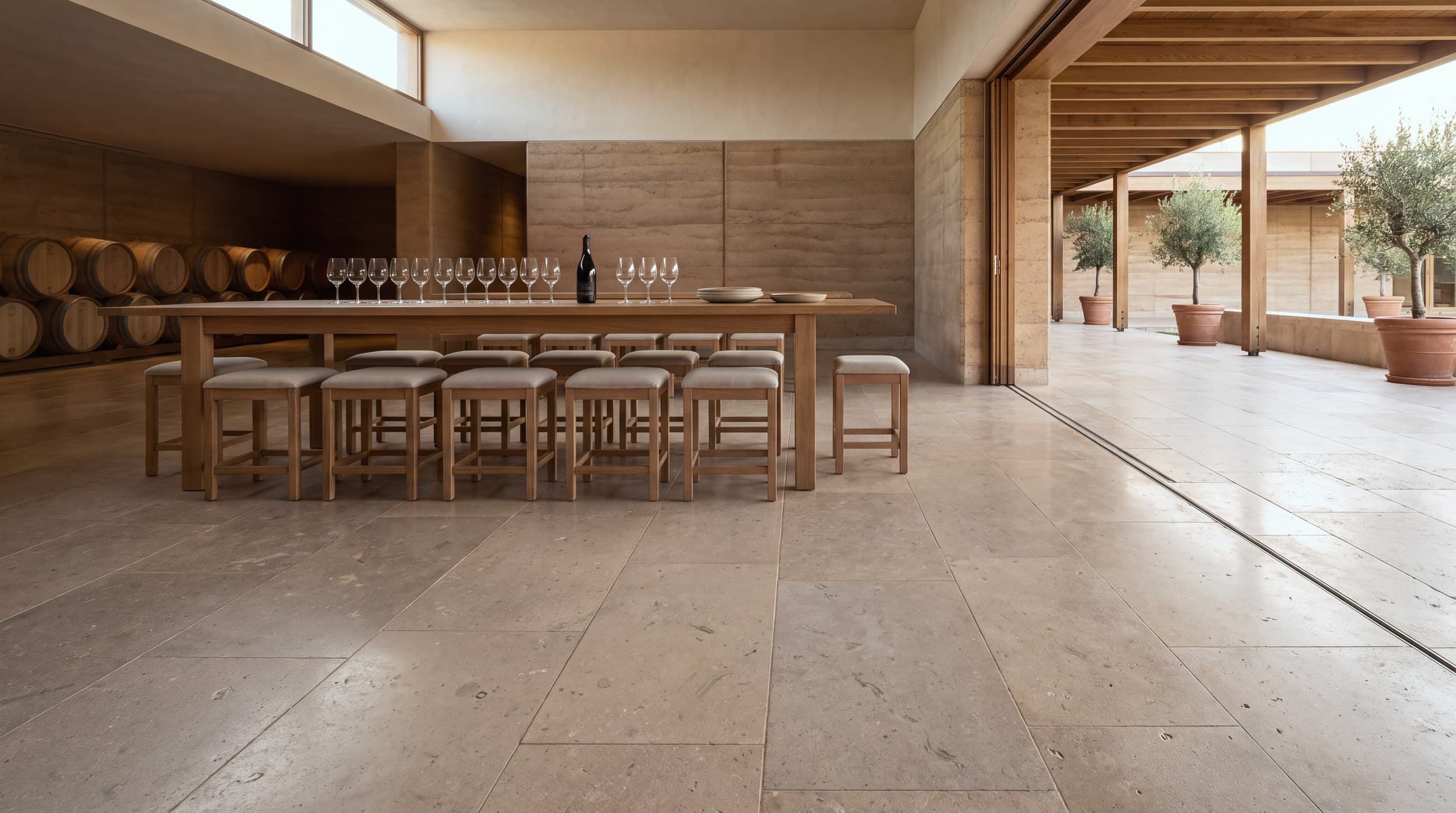 Sala de degustación de una bodega con piso continuo de piedra caliza en placas grandes, mesa larga y barricas al fondo