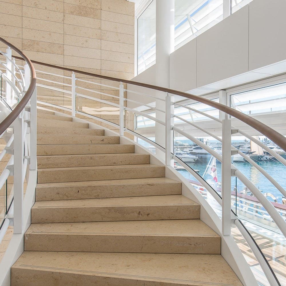 Escalera curva con pisadas de Jura Beige en un espacio de doble altura