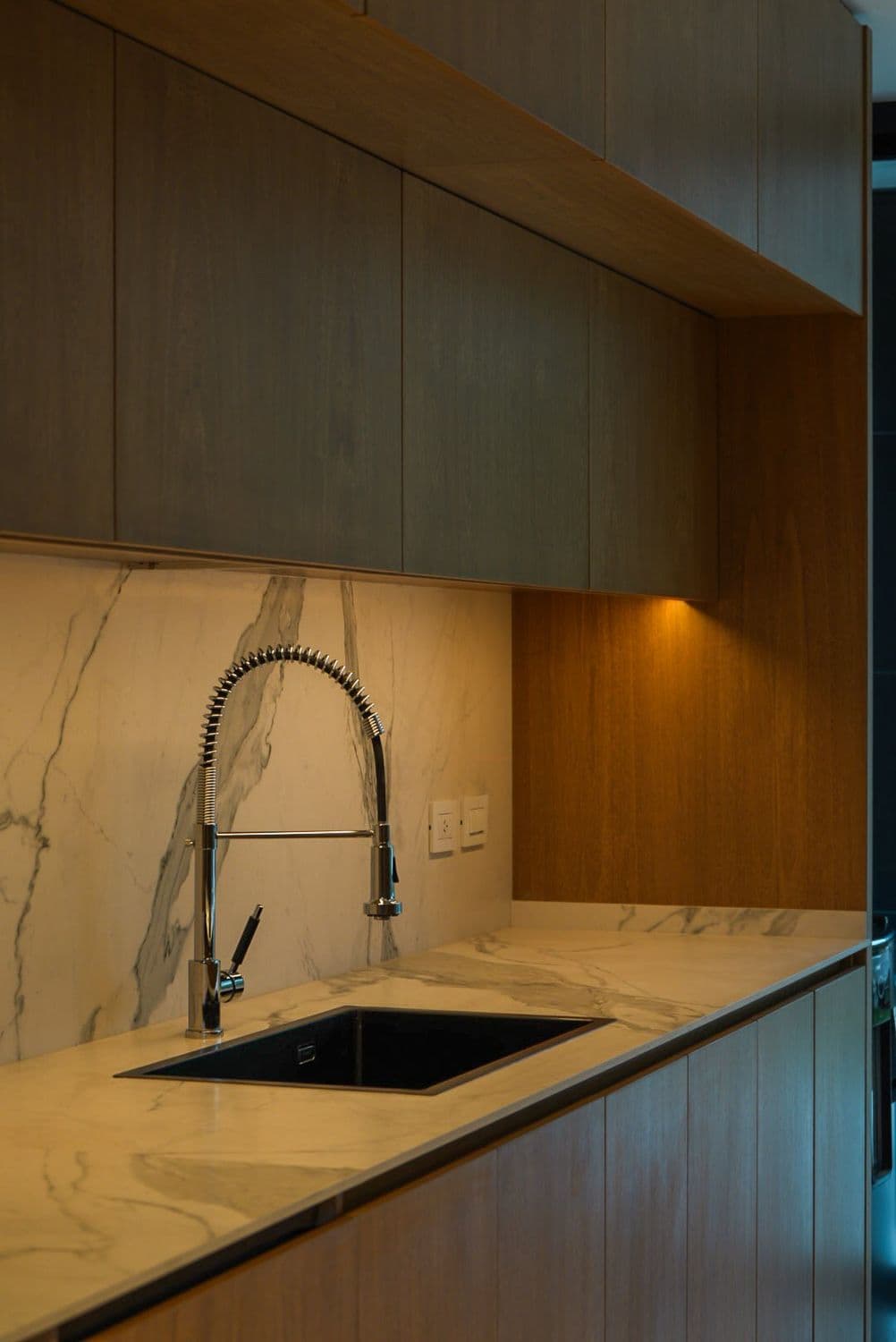 Cocina con mesada y salpicadero de mármol veteado, frentes de madera y luz cálida