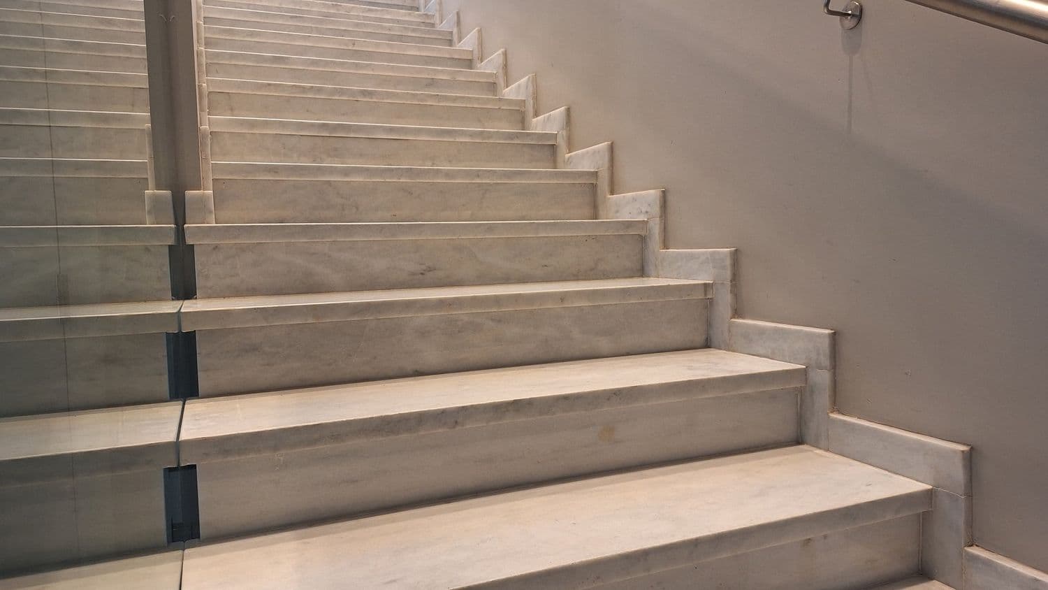 Escalera de travertino con baranda de vidrio, con el despiece de las pedadas a la vista